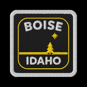 May include: Embroidered patch featuring the words "BOISE" and "IDAHO" in white, set against a black background. A yellow star and tree are also present. The patch has a yellow border and a white stitched edge.