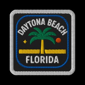 May include: Embroidered patch featuring "DAYTONA BEACH FLORIDA" in white text. The design includes a palm tree, a yellow strip, a star, and an orange circle, all set against a black background with a blue border and a gray stitched edge.