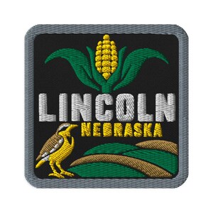 Puede incluir: Un parche bordado cuadrado con fondo negro y borde gris. Presenta una mazorca de maíz amarilla con hojas verdes, el texto blanco LINCOLN, el texto amarillo NEBRASKA, un tordo amarillo y marrón, y colinas verdes y marrones onduladas.