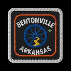 Peut inclure: Écusson brodé avec le texte "BENTONVILLE ARKANSAS" en blanc, au-dessus et en dessous d'une roue de chariot bleue et d'une rivière jaune sur fond noir. L'écusson a une bordure orange et un bord cousu blanc.