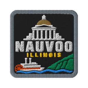 Op de afbeelding: Een vierkante geborduurde patch met een grijze rand op een zwarte achtergrond. Het toont een wit gebouw met een gouden koepel, de witte tekst NAUVOO, de gele tekst ILLINOIS, een witte stoomboot met een oranje wiel en een groene heuvel boven blauw water.