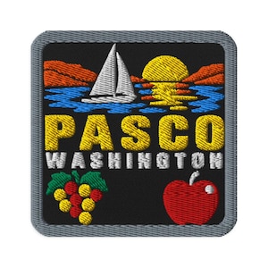 May include: A square embroidered patch with a black background featuring a white sailboat on blue water, an orange mountain range, and a yellow sun. The text PASCO WASHINGTON is embroidered in yellow and white. Below are a cluster of grapes and a red apple.