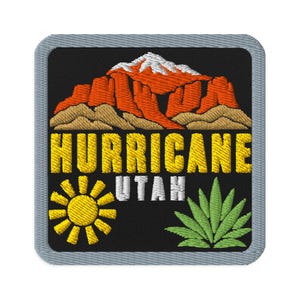 May include: A square embroidered patch with a black background featuring a red and white mountain range above the yellow text HURRICANE and white text UTAH. A yellow sun icon is on the bottom left and a green agave plant is on the bottom right.