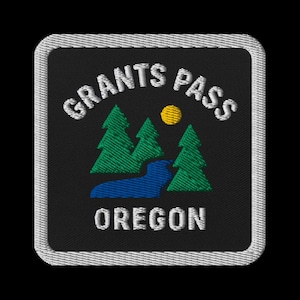 Könnte beinhalten: Gestickter Aufnäher mit dem Text "GRANTS PASS OREGON" in Weiß, der sich über einer Landschaftsszene wölbt. Die Szene zeigt grüne Bäume, einen blauen Fluss und eine gelbe Sonne vor schwarzem Hintergrund, umrahmt von einem weißen Rand.