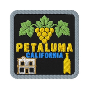 May include: A square embroidered patch with a gray border on a black background. It features a yellow grape cluster with green leaves, the yellow text PETALUMA, blue text CALIFORNIA, a white building illustration, and a yellow bottle silhouette.