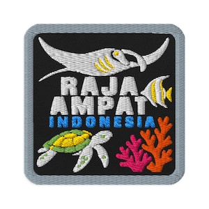 Puede incluir: Un parche bordado cuadrado con fondo negro que muestra una mantarraya blanca, un pequeño pez amarillo y blanco, una tortuga marina verde y amarilla, y coral rosa y naranja. El texto RAJA AMPAT está en blanco e INDONESIA en azul.