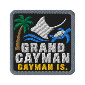 Puede incluir: Un parche bordado cuadrado con borde gris sobre fondo negro. Presenta una palmera verde, una raya blanca y una tortuga marina azul sobre olas. El texto dice GRAND CAYMAN en blanco y CAYMAN IS. en bordado de color amarillo.