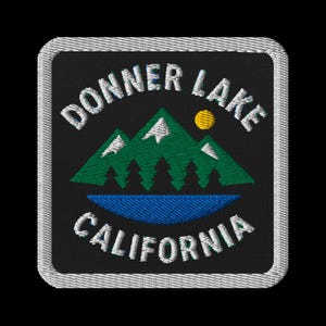 Pode incluir: Patch bordado com as palavras "DONNER LAKE CALIFORNIA" em branco, arqueadas sobre uma cordilheira verde com detalhes brancos, um sol amarelo e um lago azul. O patch tem um fundo preto e uma borda branca.
