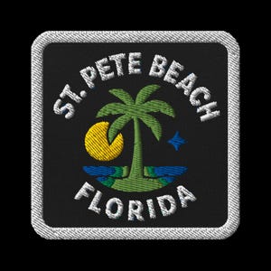 May include: Embroidered patch featuring the text "ST. PETE BEACH FLORIDA" in white, arched around a palm tree, a yellow crescent moon, and a blue star. The patch has a black background and a white stitched border.