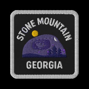 May include: Embroidered patch featuring the words "STONE MOUNTAIN GEORGIA" in white, arched over a purple mountain scene with a yellow sun and trees. The patch has a black background and a white border.