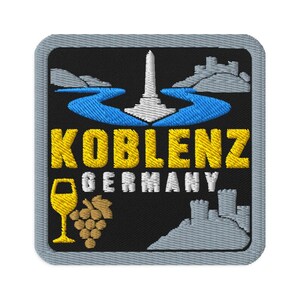 Puede incluir: Un parche bordado cuadrado con fondo negro y borde gris. Presenta un río azul, un monumento blanco y colinas grises. El texto dice KOBLENZ en amarillo y GERMANY en blanco, con una copa de vino amarilla y uvas de color marrón.