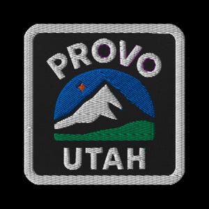 Peut inclure: Écusson brodé avec le nom "PROVO" au-dessus de "UTAH". Le motif comprend une arche bleue, une chaîne de montagnes blanche, une base verte et une petite étoile orange. L'écusson a un fond noir et une bordure blanche.