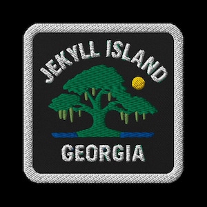 May include: Embroidered patch with a green tree, yellow sun, and blue water on a black background. White text reads "JEKYLL ISLAND" and "GEORGIA", with a white border.