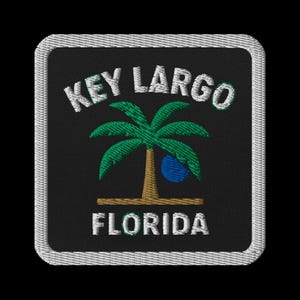 Może przedstawiać: Haftowana naszywka z napisem "KEY LARGO FLORIDA" w białym tekście. Zielona palma z brązowym pniem i niebieską kulą jest wyśrodkowana na czarnym tle. Naszywka ma białą obwódkę.