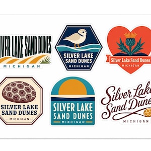May include: A collection of six stickers featuring Silver Lake Sand Dunes, Michigan. Designs include a landscape with dunes, a bird in a hexagon, a heart-shaped thistle, a patterned rock, a sunset over water, and cursive text with a honeycomb icon.