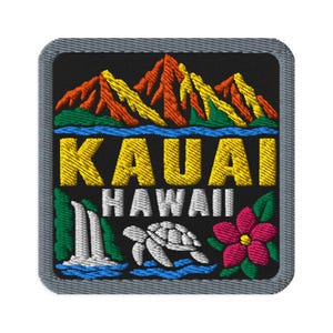 May include: A square embroidered patch with a gray border on a black background. It features orange and yellow mountains above blue water, the yellow text KAUAI, white text HAWAII, a white waterfall, a white sea turtle, and a pink hibiscus flower.