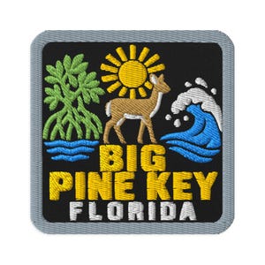 May include: A square embroidered patch with a black background and a gray border. It features a green mangrove tree, a yellow sun, a brown deer, and a blue ocean wave. The text BIG PINE KEY is in yellow, and FLORIDA is in white below it.