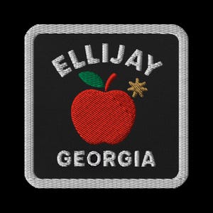 Könnte beinhalten: Gestickter Aufnäher mit dem Text "ELLIJAY GEORGIA" in Weiß, einem roten Apfel mit grünem Blatt und schwarzem Hintergrund. Der Aufnäher hat einen weißen Rand.