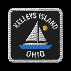 Pode incluir: Patch bordado com um veleiro em água azul, um sol amarelo e o texto "Kelleys Island Ohio" em branco. O patch tem um fundo preto e uma borda branca.