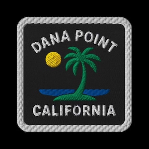 Könnte beinhalten: Gestickter Aufnäher mit dem Text "DANA POINT CALIFORNIA" in Weiß. Eine gelbe Sonne und eine grüne Palme befinden sich in der Mitte, darunter blaues Wasser. Der Aufnäher hat einen schwarzen Hintergrund und einen silbernen Rand.