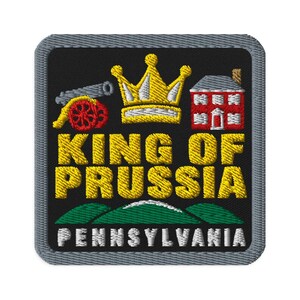 May include: A square embroidered patch with a black background and a grey border. It features a yellow crown, a red cannon, and a red building. The text reads KING OF PRUSSIA in yellow and PENNSYLVANIA in white, above green hills.