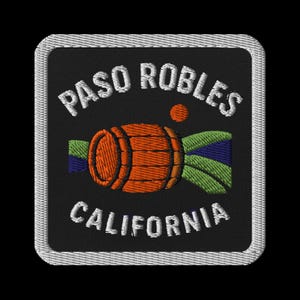 May include: Embroidered patch featuring the text "PASO ROBLES CALIFORNIA" in white, arched above and below a stylized orange barrel. A small orange circle and green and blue design are also present. The patch has a black background and a white border.