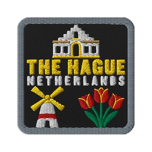May include: A square embroidered patch with a gray border on a black background. It features a white and yellow building, the text THE HAGUE NETHERLANDS in yellow and white, a white and yellow windmill, and three red and green tulips.
