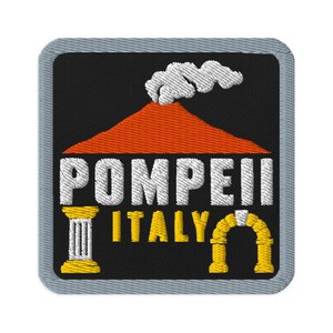 Puede incluir: Un parche bordado cuadrado con borde gris sobre fondo negro. Presenta un volcán naranja con humo blanco, el texto blanco POMPEII, el texto amarillo ITALY, acompañado de una columna blanca y un gráfico de un arco de color amarillo.