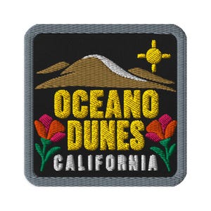 Könnte beinhalten: Ein quadratischer Stickaufnäher mit grauem Rand auf schwarzem Hintergrund. Er zeigt braune Sanddünen, eine gelbe Sonne und zwei bunte Blumen. Der Text lautet OCEANO DUNES in Gelb und CALIFORNIA in Weiß, zentriert auf dem Aufnäher.