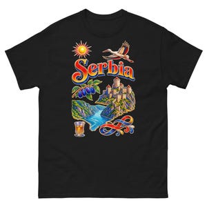 Pode incluir: Uma t-shirt preta com uma estampa gráfica colorida com o texto "Serbia" numa fonte estilizada. O design inclui um sol, uma cegonha a voar, uma fortaleza de pedra, um rio, ameixas e um copo com um líquido de cor âmbar.