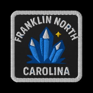 Op de afbeelding: Geborduurde patch met een zwarte achtergrond en een witte rand. De patch toont de tekst "FRANKLIN NORTH" bovenaan en "CAROLINA" onderaan. In het midden staat een cluster van blauwe kristallen met witte punten en een gouden ster.