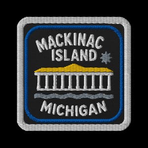 May include: Embroidered patch featuring the words "MACKINAC ISLAND MICHIGAN" in white, with a yellow-roofed building and wavy lines. The patch has a black background, blue border, and white stitching.