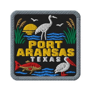 Op de afbeelding: Een vierkante geborduurde patch met een zwarte achtergrond met een gele zon, een witte reiger, groen riet en blauw water. De tekst luidt PORT ARANSAS in het geel en TEXAS in het wit, met een rode vis en een witte pelikaan onderaan.
