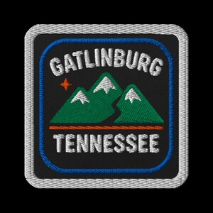 Könnte beinhalten: Gestickter Aufnäher mit dem Text "GATLINBURG TENNESSEE" in Weiß, über einer Grafik von drei grünen Bergen mit weißen Schneekappen. Ein kleiner orangefarbener Stern befindet sich über den Bergen. Der Aufnäher hat einen schwarzen Hintergrund mit einem blauen und weißen Rand.