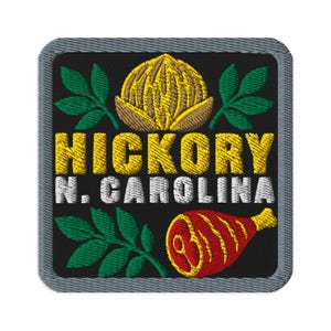 May include: A square embroidered patch with a black background and a grey border. It features a yellow hickory nut, green leaves, and a red ham. The text HICKORY is in yellow, and N. CAROLINA is in white, centred between the graphic elements.