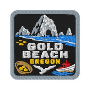 May include: A square embroidered patch with a black background featuring a white mountain arch, blue ocean waves, and a red and white boat. The text reads GOLD BEACH OREGON in white and yellow. Includes a tan basket with gold nuggets and a white bird.