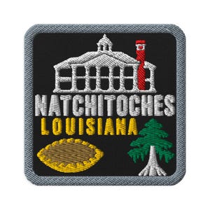Op de afbeelding: Een vierkante geborduurde patch met een zwarte achtergrond en een grijze rand. Het toont een wit gebouw met een rode schoorsteen, de tekst NATCHITOCHES LOUISIANA in wit en geel, een gele taart en een groene cipres met een witte stam.