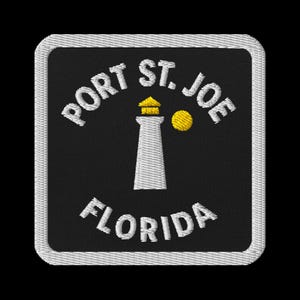Puede incluir: Parche bordado con un faro blanco, techo amarillo y círculo amarillo sobre fondo negro. El texto "PORT ST. JOE FLORIDA" es blanco. Con borde blanco.