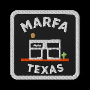 May include: Embroidered patch featuring the text "MARFA TEXAS" in white, arched at the top and bottom. A white building with "PRADA" above it is in the center, with a small cactus and a sun graphic.