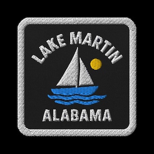 May include: Embroidered patch featuring a sailboat on blue waves under a yellow sun. The text "LAKE MARTIN ALABAMA" is arched above and below the image. The patch has a black background with a white stitched border.