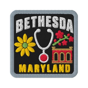 Peut inclure: Un écusson brodé carré avec un fond noir et une bordure grise. Il présente le texte blanc BETHESDA en haut et MARYLAND en jaune en bas. Le motif comprend une fleur jaune, un stéthoscope blanc et un bâtiment rouge sur le devant.