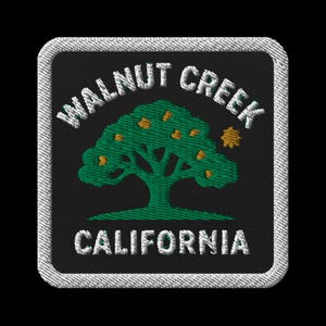 May include: Embroidered patch featuring the words "WALNUT CREEK CALIFORNIA" in white, arched around a green tree with orange accents. The patch has a black background and a white stitched border.