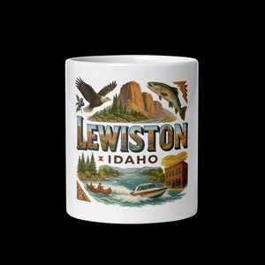 Könnte beinhalten: Weißer Keramikbecher mit farbenfrohem Design mit dem Text "Lewiston Idaho". Das Design umfasst einen Adler, einen Fisch, Berge, einen Fluss, ein Boot und ein Gebäude. Der Becher ist zylindrisch und hat einen schwarzen Hintergrund.