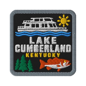 Puede incluir: Un parche bordado cuadrado con borde gris sobre fondo negro. Presenta una casa flotante blanca sobre agua azul, un sol amarillo, tres pinos verdes y un pez naranja. El texto dice LAKE CUMBERLAND en blanco y KENTUCKY en color amarillo.