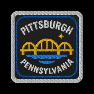 May include: Embroidered square patch featuring the city name "PITTSBURGH" and state name "PENNSYLVANIA" in white, arched text. A yellow bridge design is centered above blue water. A small yellow star is to the right of the bridge.