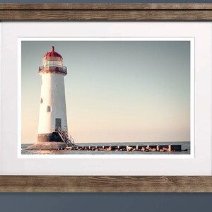 May include: A white lighthouse with a red roof stands on a rocky outcropping in the water. The lighthouse is surrounded by a series of breakwaters.