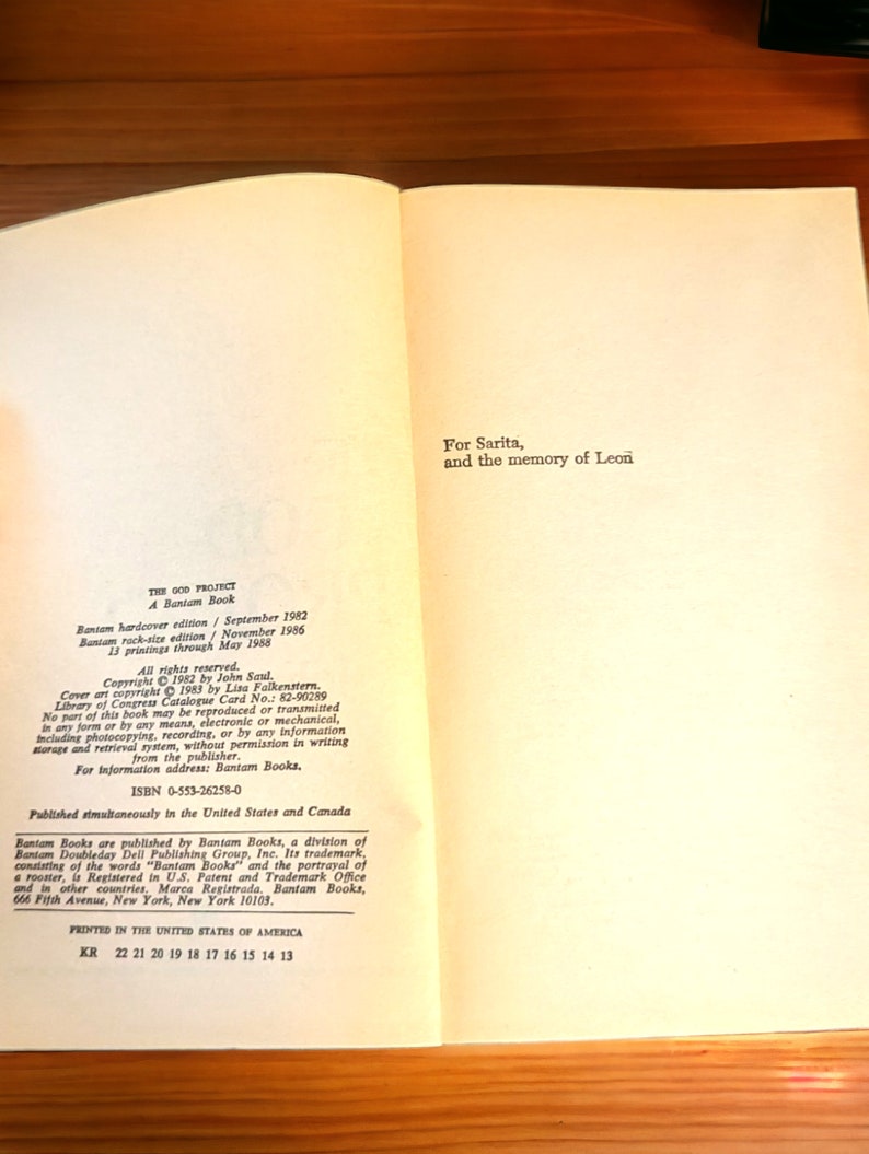 May include: Open book with text from "THE GOD PROJECT" by John Saul. The book is a Bantam hardcover edition from September 1982. The text includes copyright information, ISBN, and the publisher's address in New York.