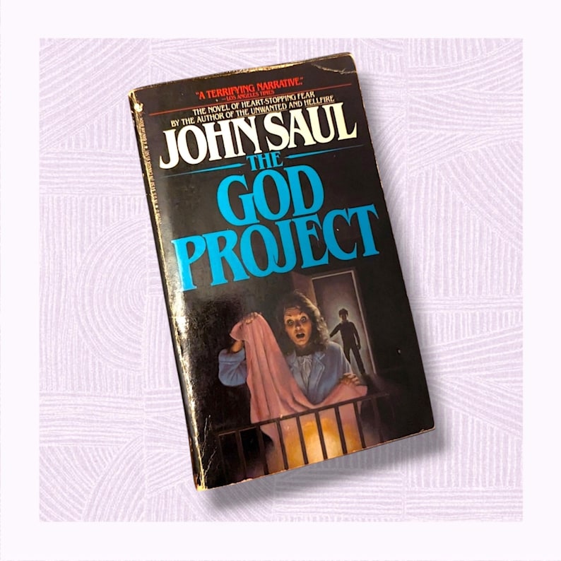 May include: A vintage paperback book titled "The God Project" by John Saul. The cover features a dark background with blue and white text. An illustration depicts a woman holding a pink cloth, with a shadowy figure in the background.