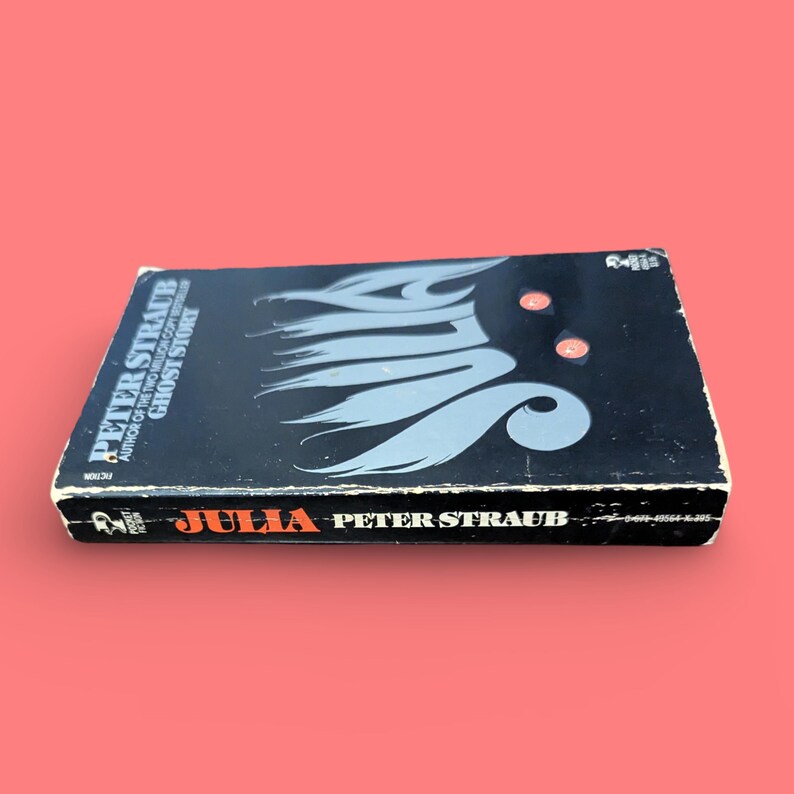 May include: A black paperback book titled "Julia" by Peter Straub. The book cover features a silver illustration of the word "Julia" with a stylized flame design.