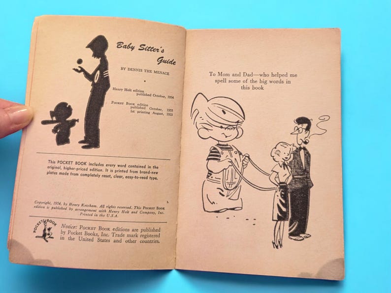 May include: A vintage book titled "Baby Sitter's Guide" by Dennis the Menace. The book has a black and white illustration of a child holding a leash with two other children. The book cover includes publication dates and information about the Pocket Book edition.